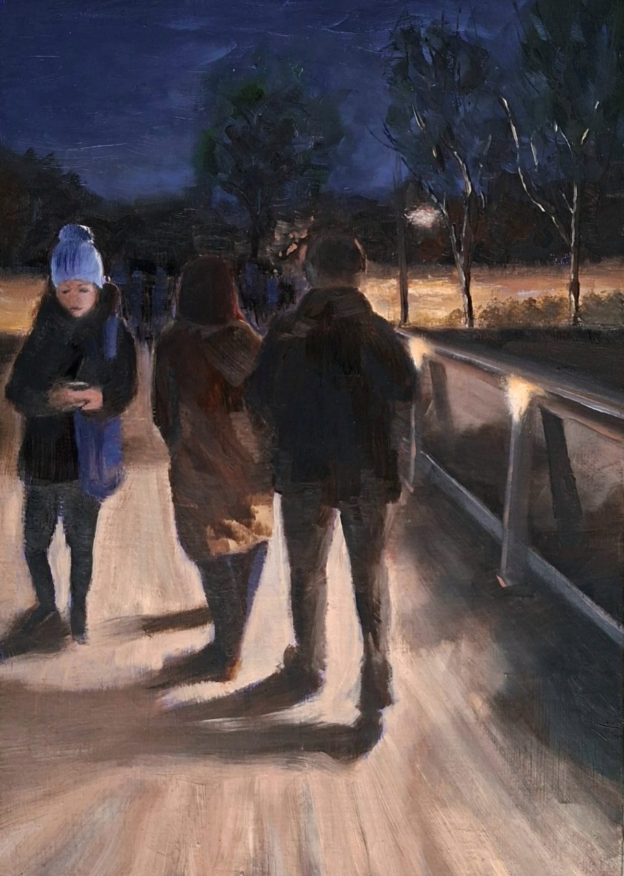 Ein paar auf einer beleuteten Brücke mit Holzplanken. Eine entgegenkommende Frau mit einer Pudelmütze schaut auf ihr Handy.