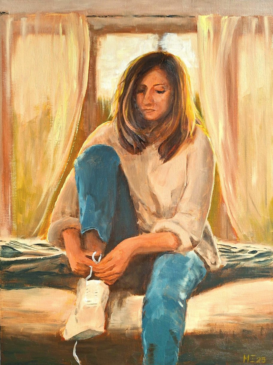 Eine Frau in Jeans sitzt auf dem Bett in einem sonnendurchfluteten Schlafzimmer und zieht sich die Schuhe an.